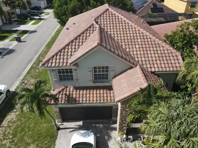 Red barrel tile roof on a two-story house above a garage and palm-lined driveway in Atlantis, photographed July 2025