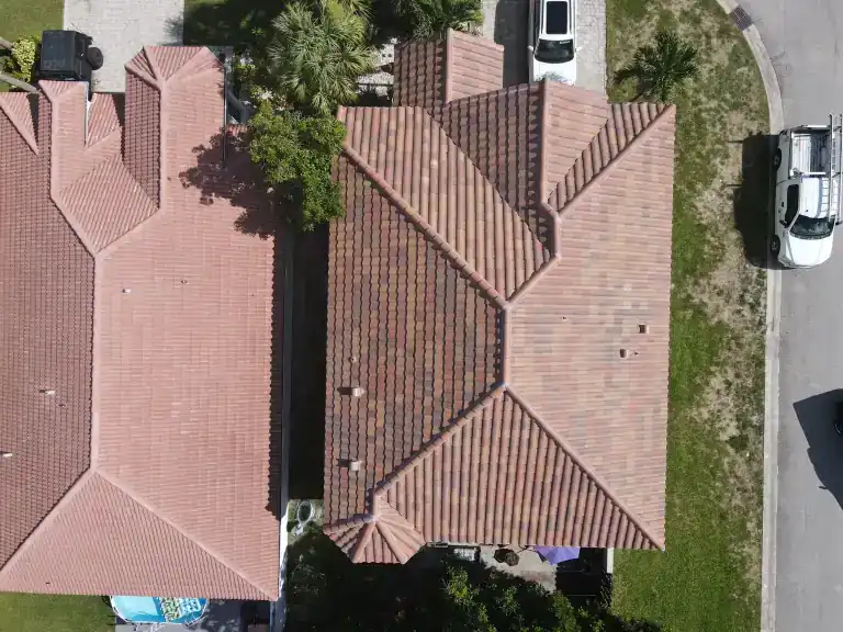 Vista cenital de un techo rojo de tejas a cuatro aguas en una casa entre un techo vecino y una calle residencial en Atlantis, fotografiado en julio de 2025
