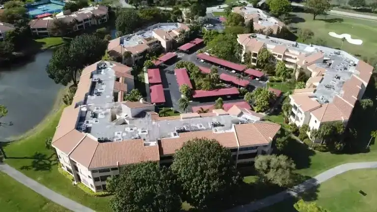 Flat roof sections and tan tile edges around a condominium courtyard beside a lake and golf course in La Paz, Boca Raton