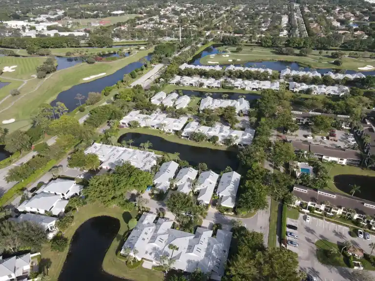 White tile roofs across a golf community with branching canals and long rows of homes in Waters Edge, Boca Raton