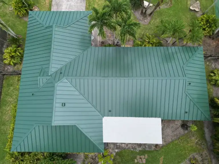 Top-down drone view of a green standing seam metal roof with a white flat section on a single-story house in Boynton Beach