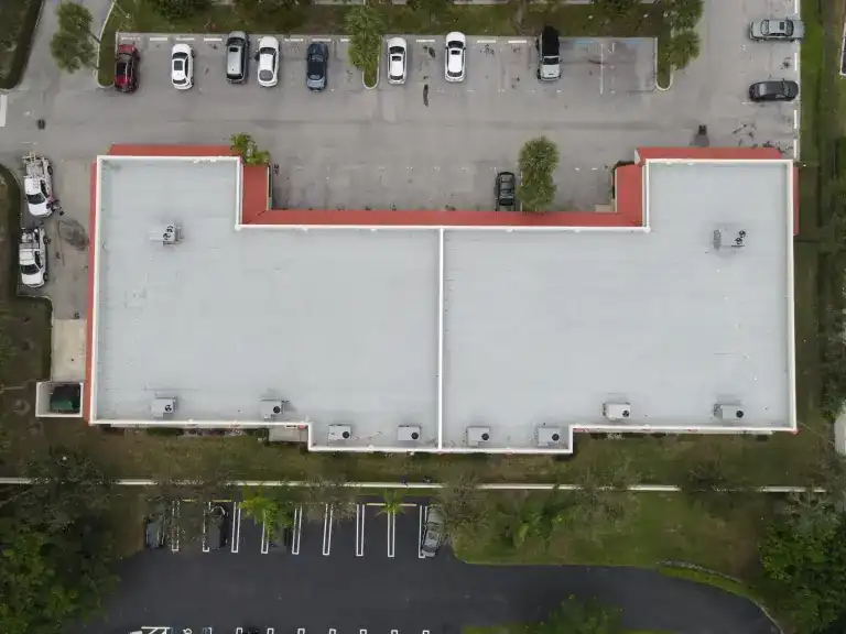 Overhead view of a broad white flat roof with recessed frontage between two parking lots in Delray Beach, photographed November 2024