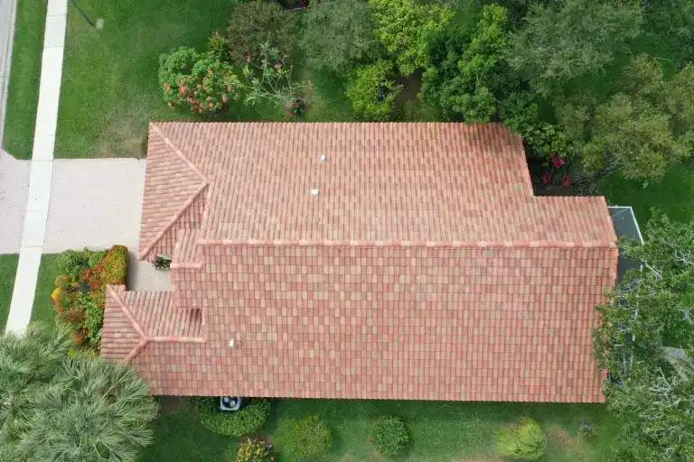 Overhead view of a red tile roof with a long central ridge beside lawn and leafy trees in Vía Verona, Delray Beach, photographed April 2023