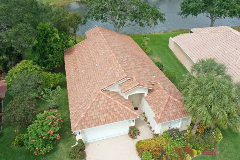 Red tile roof over a one-story lakeside house with a white garage and flowering front garden in Vía Verona, Delray Beach, photographed April 2023