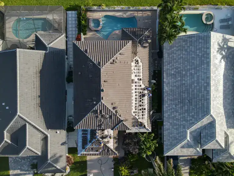 Straight-down view of tile replacement on a narrow house between neighboring roofs and backyard pools in Delray Beach, photographed August 2026