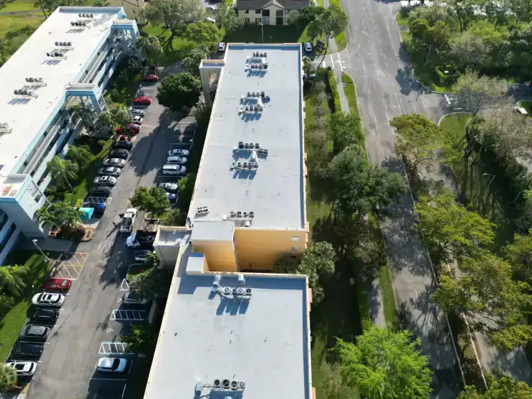 White flat roofs on apartment buildings beside a road and parking areas in Greenacres, photographed March 2024