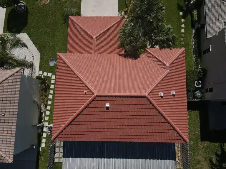 Overhead view of a red tile roof with stepped hip sections between neighboring houses and lawn in Greenacres, photographed July 2025