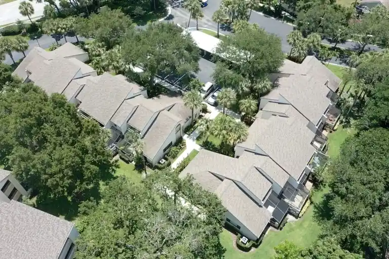 Two rows of pale shingle roofs around a tree-filled courtyard with lawns and walkways in Juno Beach