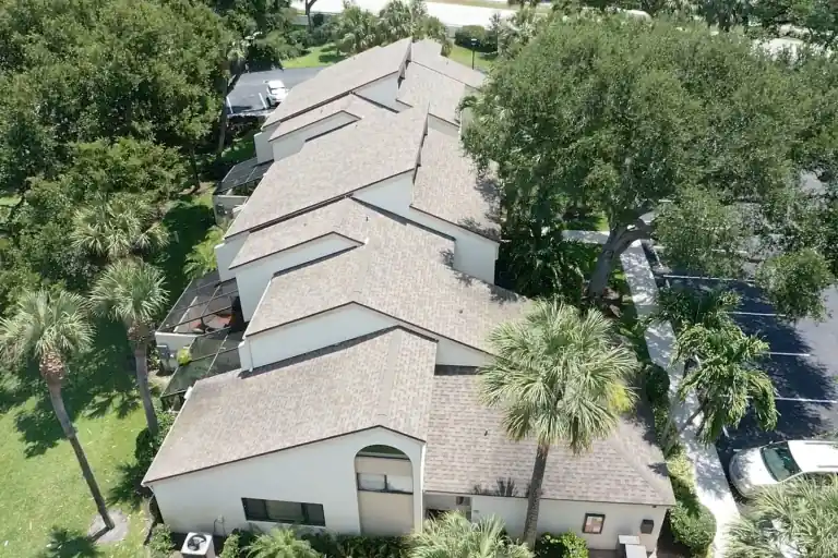Elevated view of stepped shingle gables above attached homes beside a shaded parking lane and tall palms in Juno Beach
