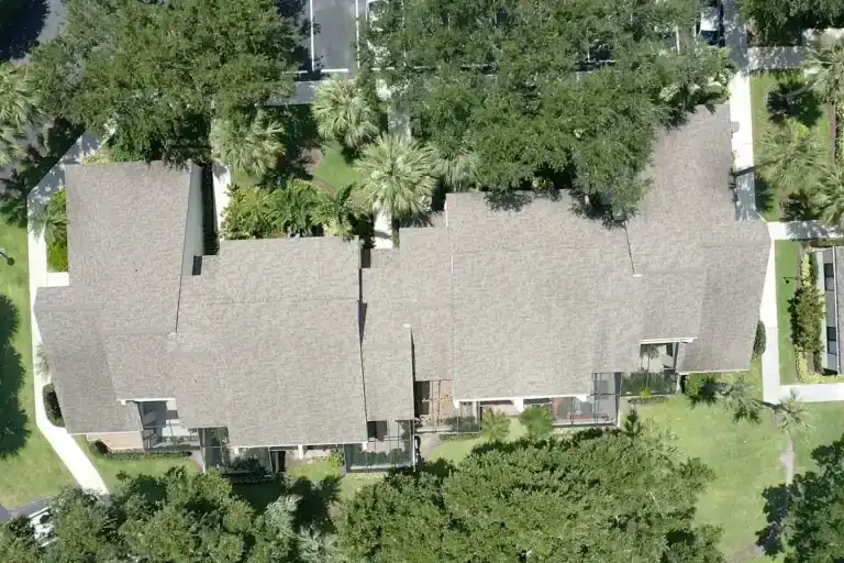 Straight-down view of a long shingle roof with two projecting wings, rear patios and a white walkway along the left end in Juno Beach