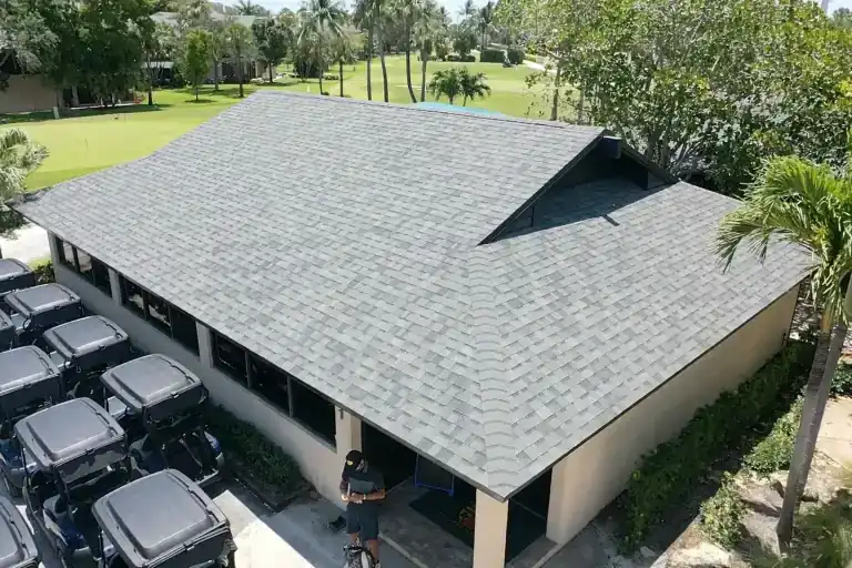 Gray shingle roof with a raised central gable above an open-sided building and rows of golf carts beside a green lawn in Jupiter