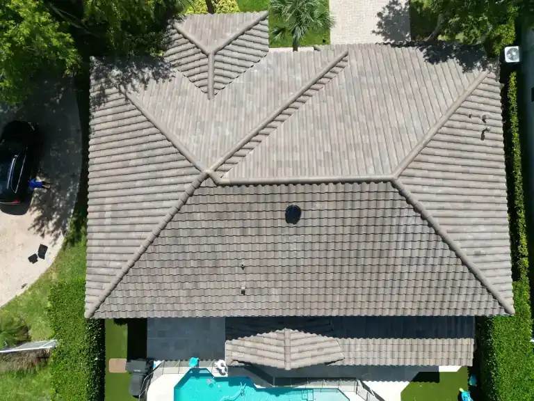 Top-down drone view of a brown flat tile hip roof on a house with a pool and a screened enclosure in Jupiter