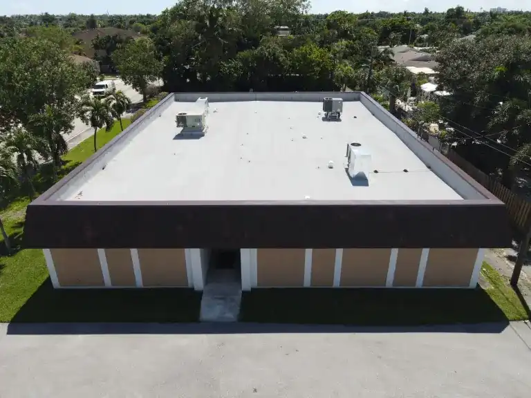 White flat roof with two rooftop units on a low rectangular building behind a striped facade and lawn in Lake Worth Beach, photographed October 2024