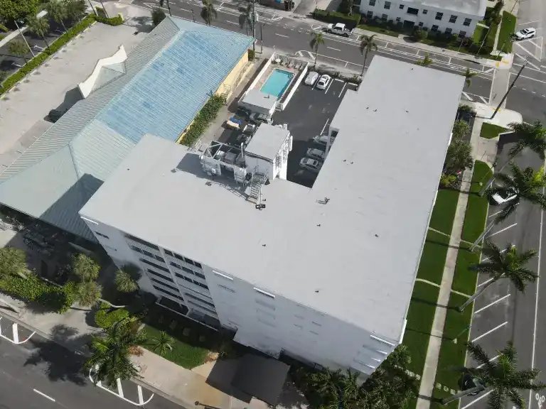 White flat roof on a waterfront condominium tower beside a swimming pool in Lake Worth Beach, photographed June 2025