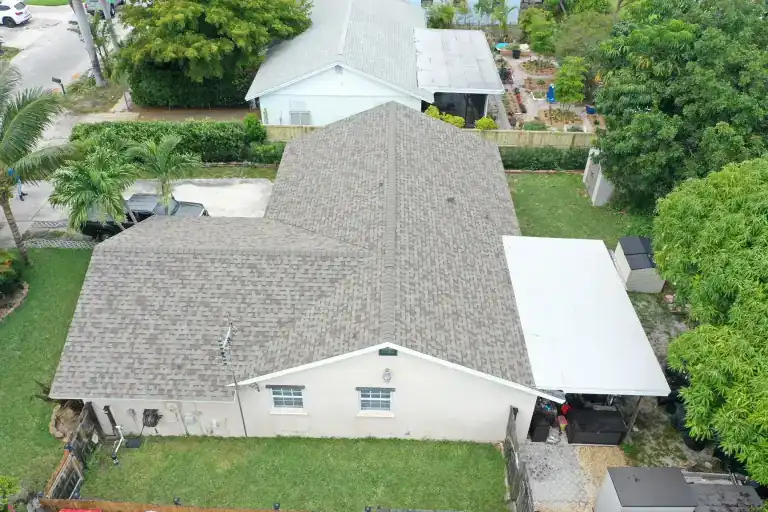 Drone view of a gray architectural shingle roof with a white flat porch roof on a single-story house with a lawn in Lantana