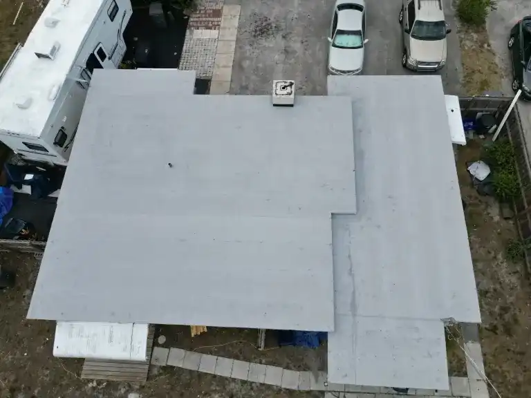 Light gray flat roof with stepped edges and a square vent beside parked cars and a recreational vehicle in North Palm Beach