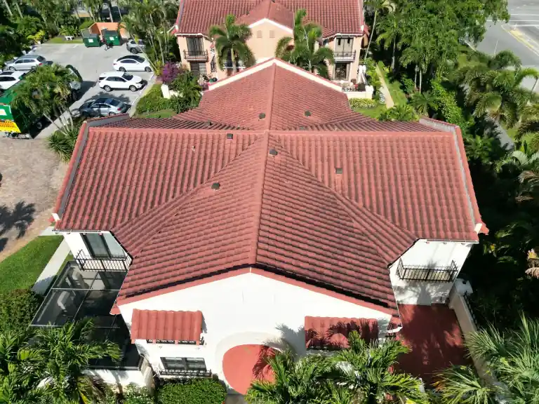Red tile roof with intersecting hips above a white building with balconies and a curved entrance, surrounded by palms in North Palm Beach