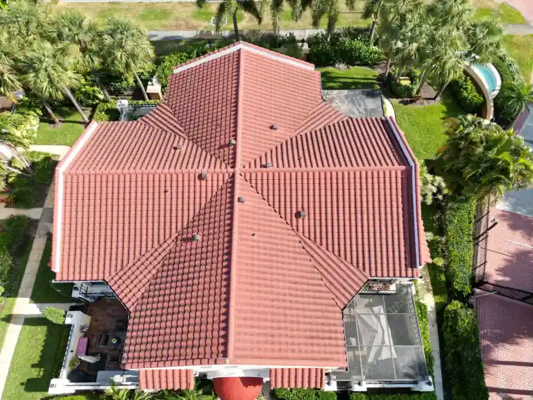 Overhead view of a red tile roof with a long central ridge, dark vents and a screened patio beside palms in North Palm Beach