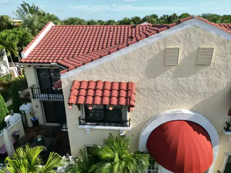 Drone view of a red barrel tile roof with a tiled turret above a stucco house with balconies and a striped awning in North Palm Beach