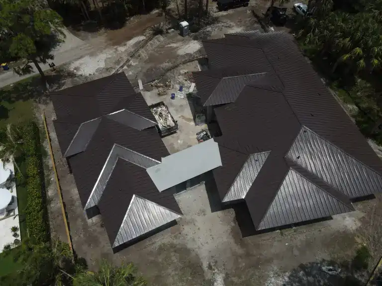 Vista oblicua elevada de alas de techo de metal oscuro alrededor de un patio arenoso en una casa en construcción, fotografiado en mayo de 2026