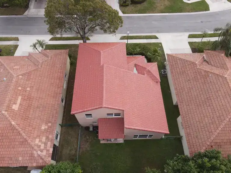 Rear aerial view of a pink house with a red tile roof and small covered patio between two neighboring tile roofs in Palm Beach Gardens