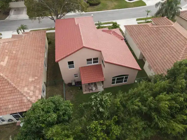 Drone view of a salmon-pink flat tile roof on a two-story house among tile-roofed neighbors and trees in Palm Beach Gardens