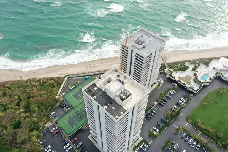 White tower roofs with rooftop equipment above tennis courts beside breaking ocean waves in Riviera Beach