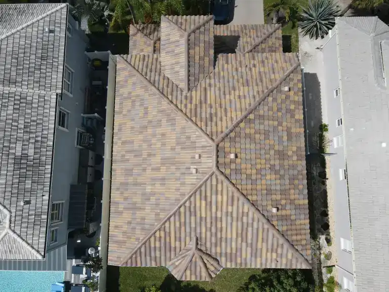 Vista desde arriba de un techo de tejas jaspeadas color arena con cumbreras cruzadas entre dos techos vecinos largos en Royal Palm Beach, fotografiado en agosto de 2025