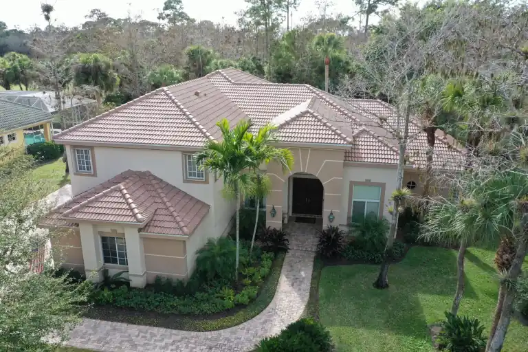 Tan tile roof on a single-story house with a curved driveway and palms in Wellington, photographed February 2023