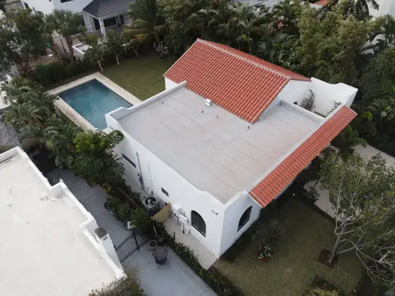 White flat roof and red tile roof sections on a home beside a swimming pool in West Palm Beach, photographed December 2024