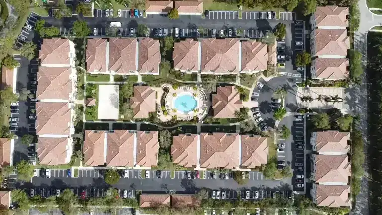 Top-down view of pink tile roofs around a condominium courtyard with a circular blue pool in West Palm Beach