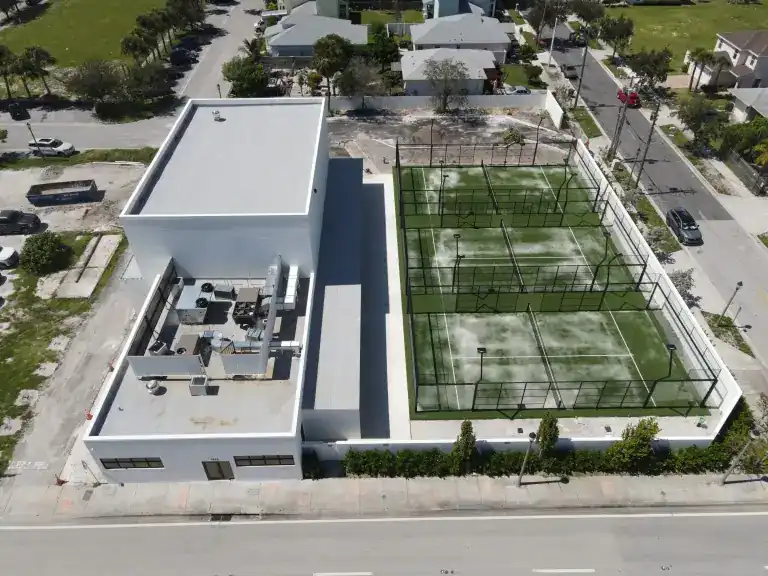 White flat roof and rooftop equipment on a sports facility with two fenced courts along a street in West Palm Beach, photographed October 2024
