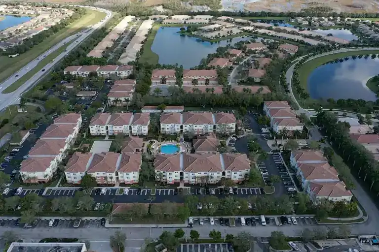 Red tile apartment roofs around a pool courtyard with lakes and rows of homes beyond in West Palm Beach