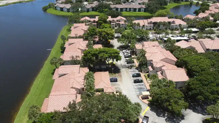 Pink tile roofs on apartment buildings along a lake, with palms and parked cars between them in Sterling Villages, West Palm Beach