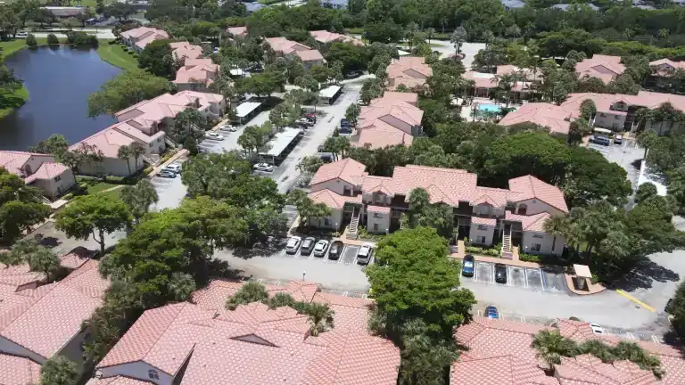 Wide view of pink tile apartment roofs across a wooded neighborhood with curving parking lanes in Sterling Villages, West Palm Beach