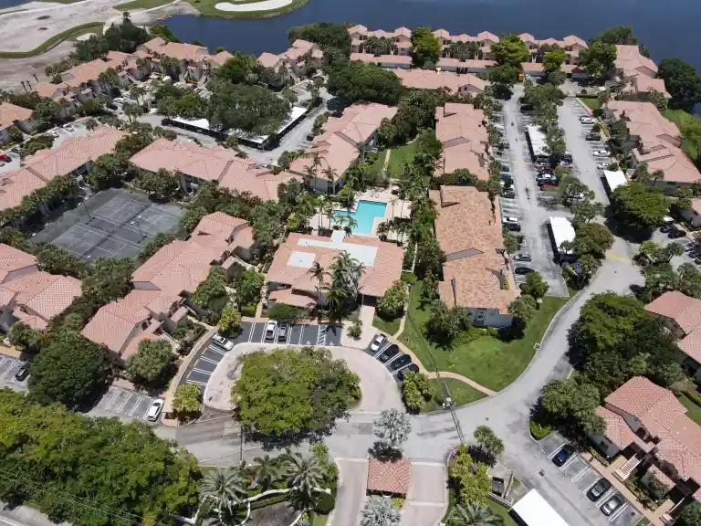 Pink tile roofs around a community pool, tennis courts and a landscaped entrance roundabout in Sterling Villages, West Palm Beach, completed June 2026