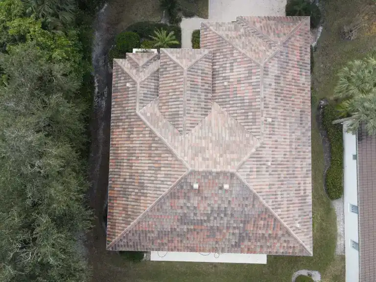 Overhead view of a multicolored tile roof on a house surrounded by trees in West Palm Beach, photographed January 2025