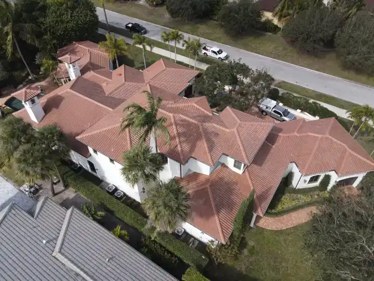 Terracotta tile roof with many intersecting hips over a white house beside a street and tall palms in West Palm Beach, photographed January 2025