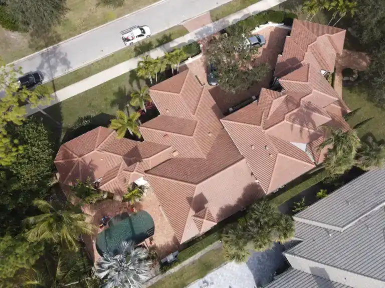 High oblique view of a sprawling red tile roof wrapping around a brick courtyard and mature trees in West Palm Beach, photographed January 2025